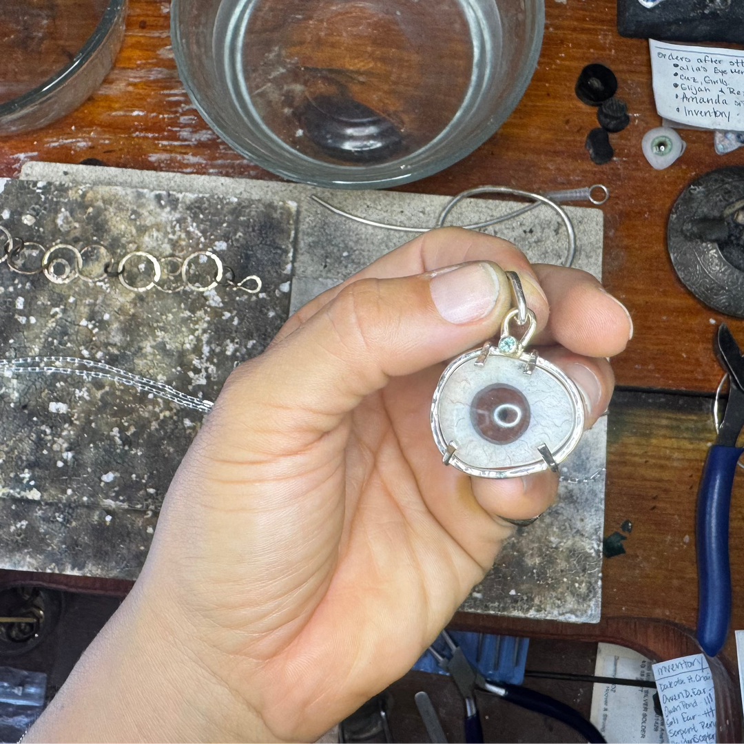 Hand holding a small metal object on a cluttered workbench with tools and materials.